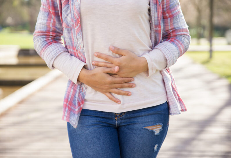 Woman suffering from bellyache. Cropped portrait of girl walking outdoors and keeping hands on stomach. Stomach ache concept